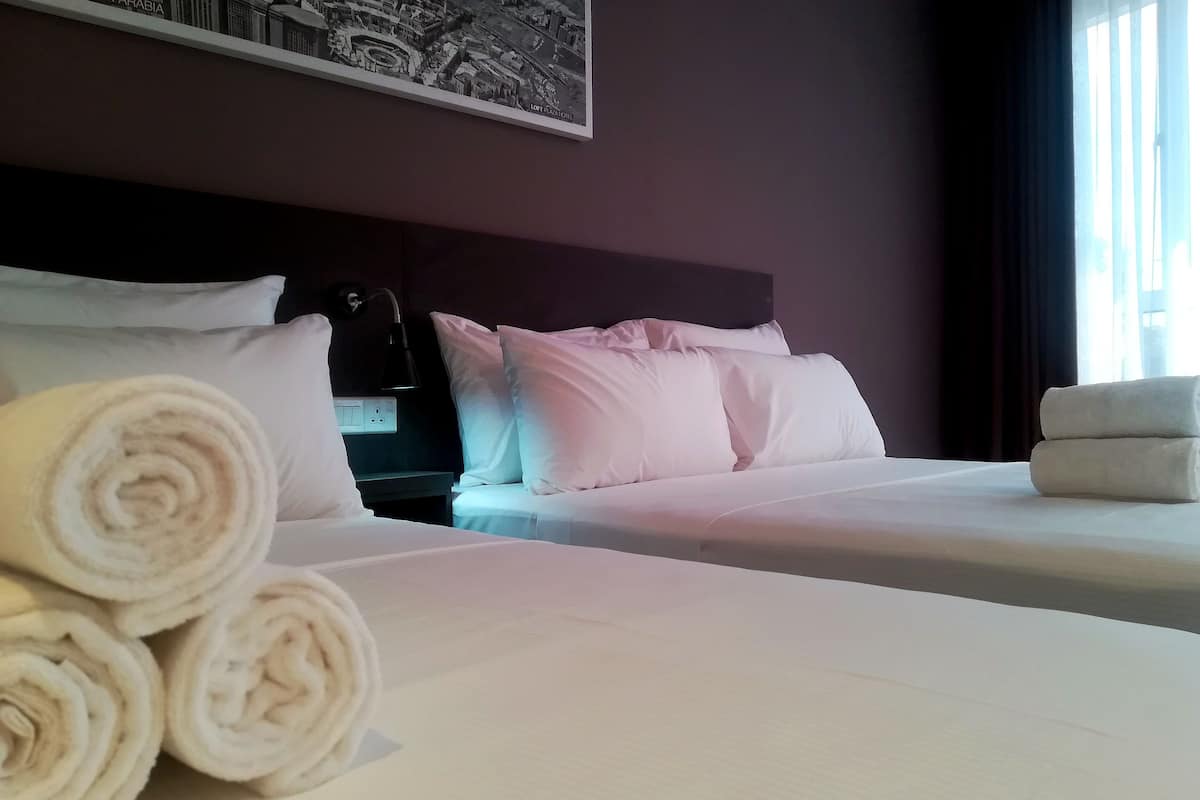 A hotel room with two beds, white linens, rolled towels, a dark headboard, and a framed picture on the wall.