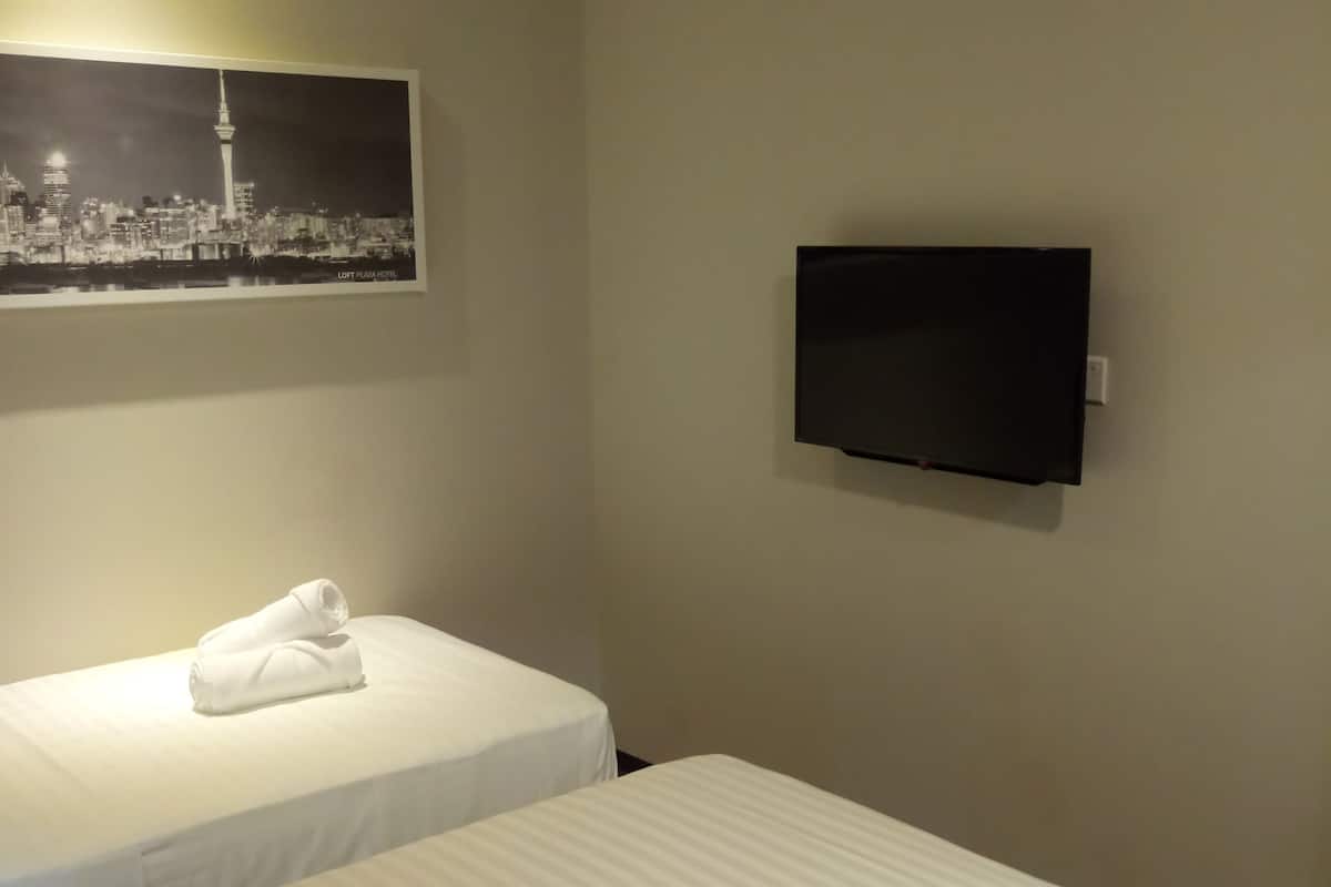 A hotel room with two beds, a flat-screen TV mounted on the wall, and a cityscape picture above the beds.
