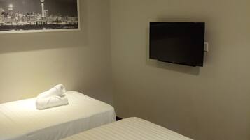 Habitació d'hotel amb dos llits, un televisor de pantalla plana fixat a la paret i una fotografia de paisatge urbà sobre els llits.