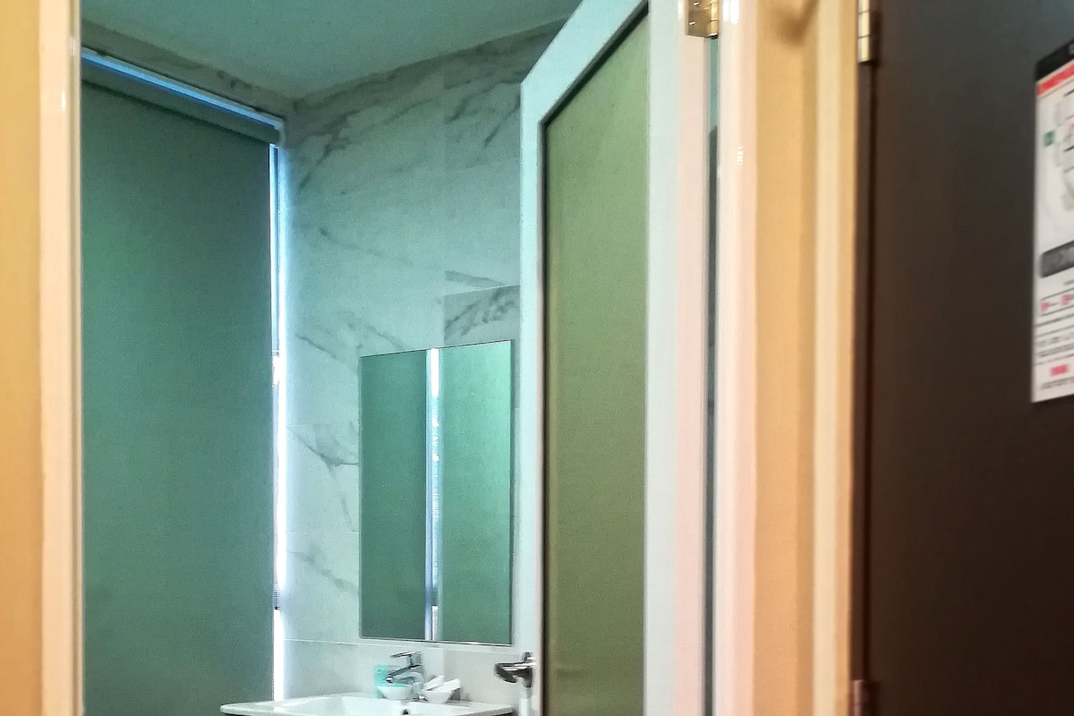 A narrow hallway leading to a bathroom with a marble wall, a sink, and a mirror.