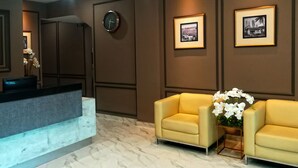 A reception area with a marble floor, a reception desk, two yellow armchairs, a clock, and framed pictures on the wall. - The Loft Plaza Hotel (Kajang)