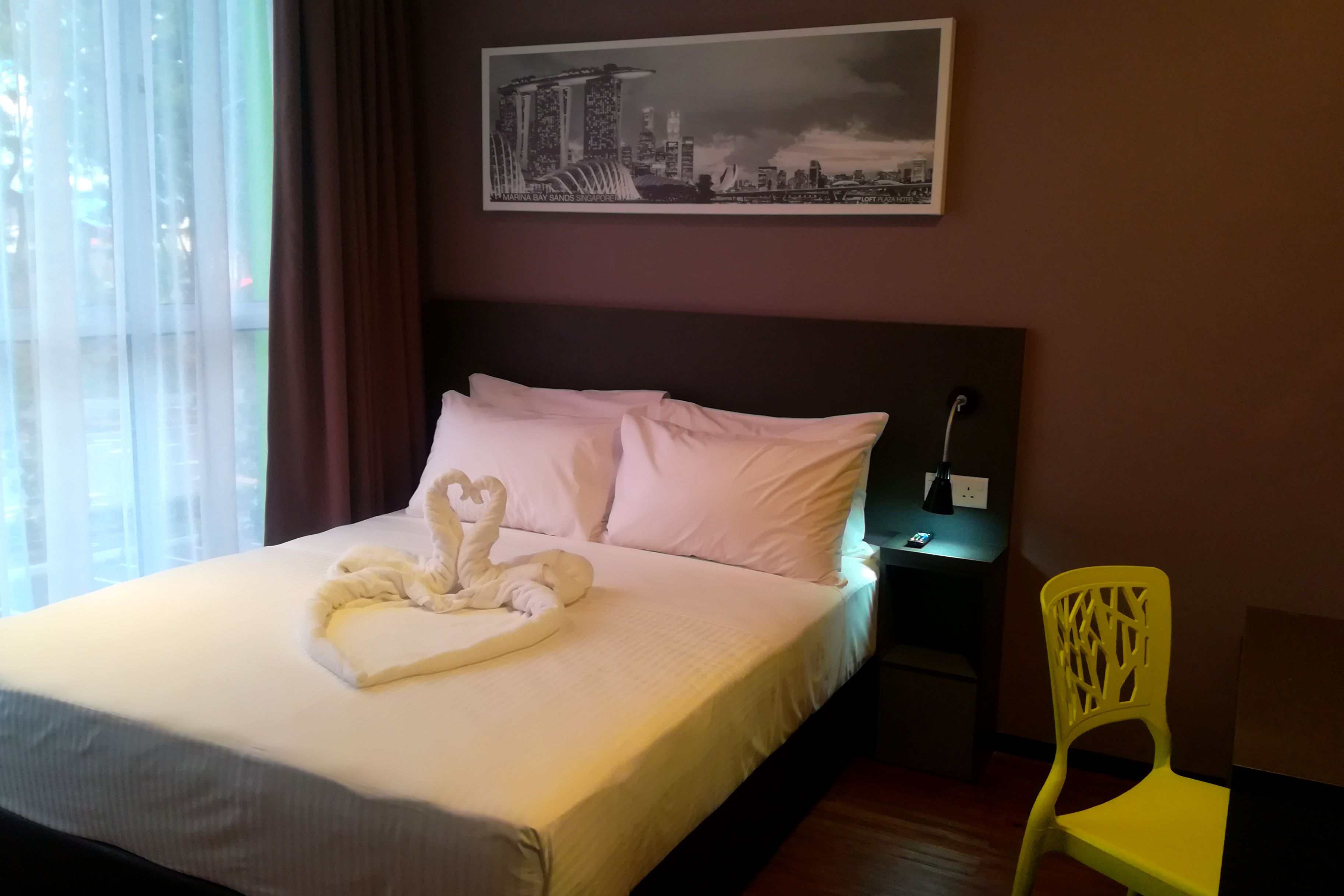 Un letto rifatto con cura, un asciugamano a forma di cuore e un quadro con una veduta sulla città.