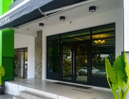 A hotel entrance with a black awning, large glass doors, and a visible car parking area.