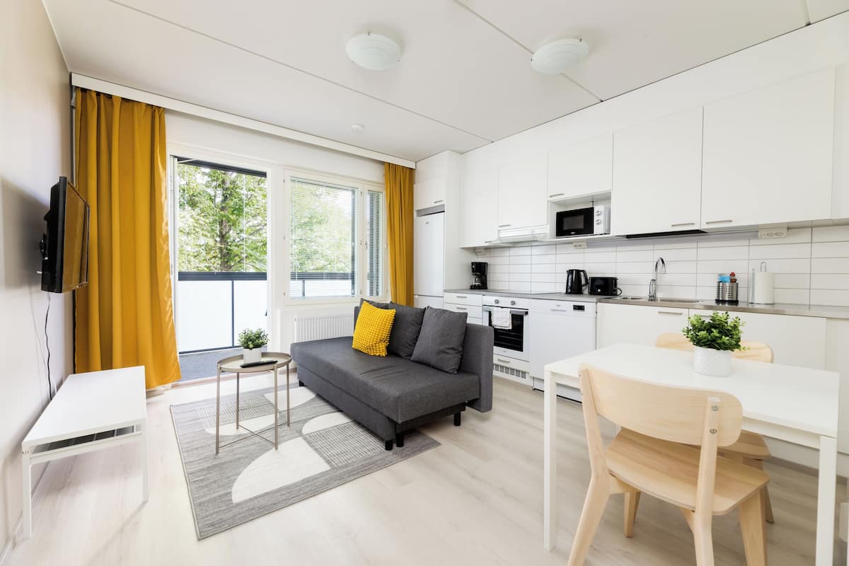 A modern kitchen with white cabinets, a microwave, and a stove. There is a dining table with chairs and a sofa with cushions.
