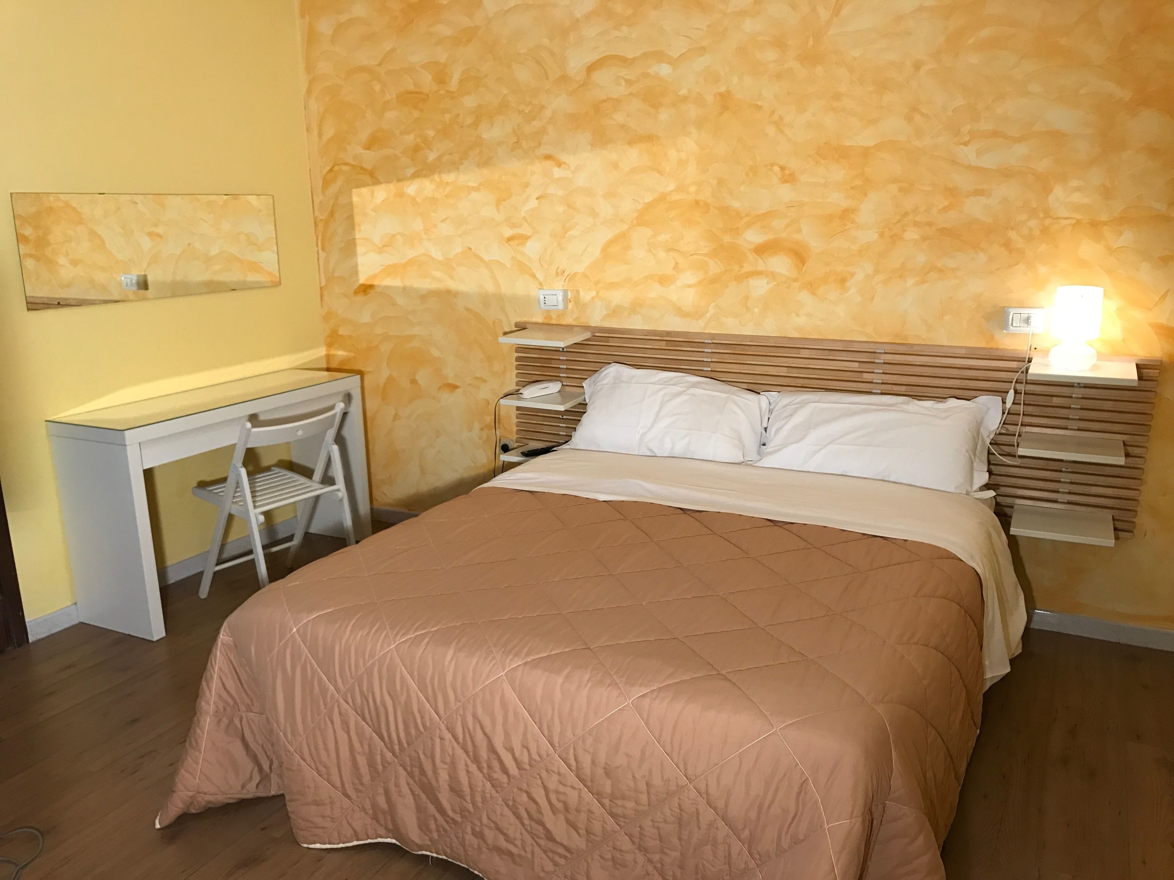 A hotel room with a bed, bedside tables, a desk, and a chair.