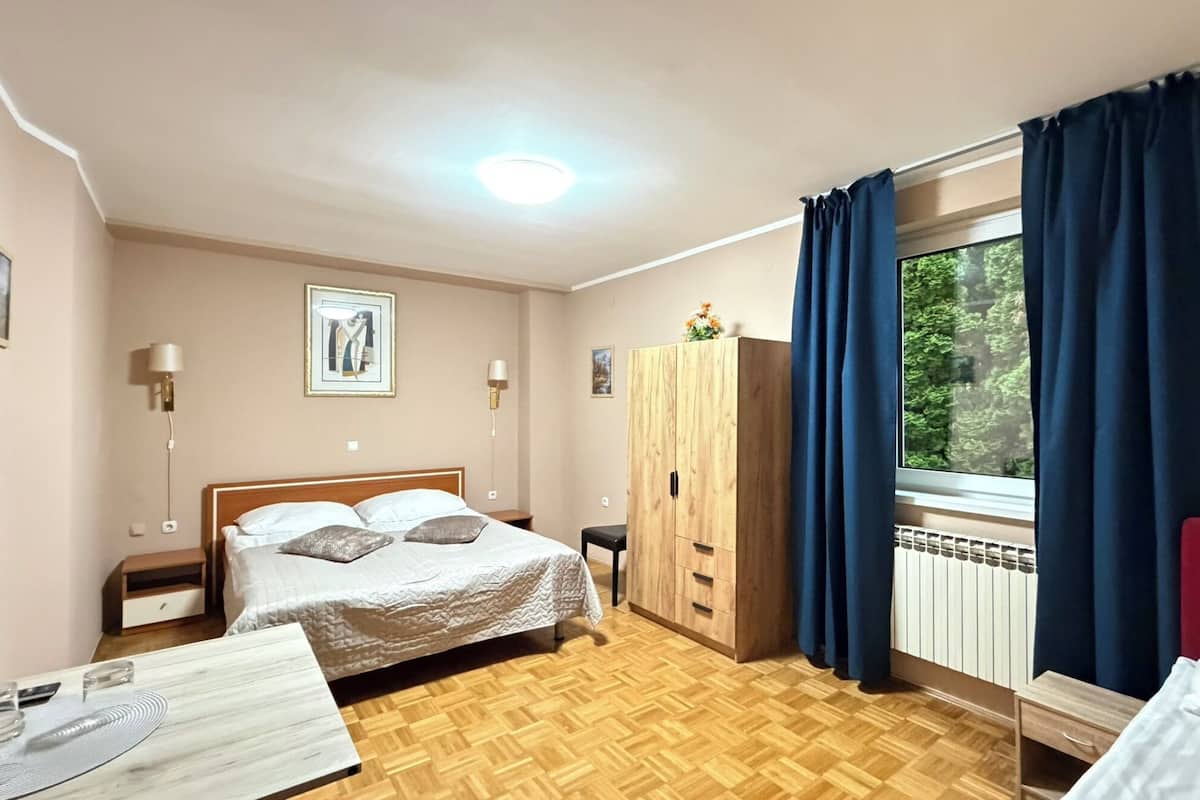 Ein Schlafzimmer mit Bett, Kleiderschrank, Schreibtisch und einem fensterbepflanzten Fenster.