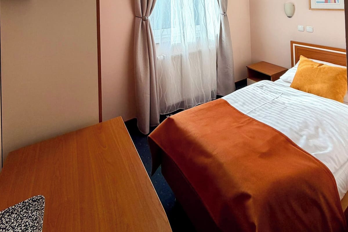 Ein Hotelzimmer mit Bett, Schreibtisch, Fernseher, einem Fenster mit Vorhängen und einer Wandleuchte.