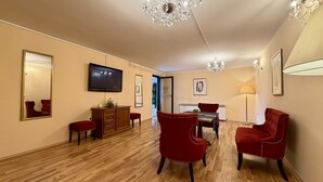 A hotel room with a wooden floor, a television, a mirror, a red chair, a wooden cabinet, and a chandelier. - Hotel Imperium (Moravske Toplice)
