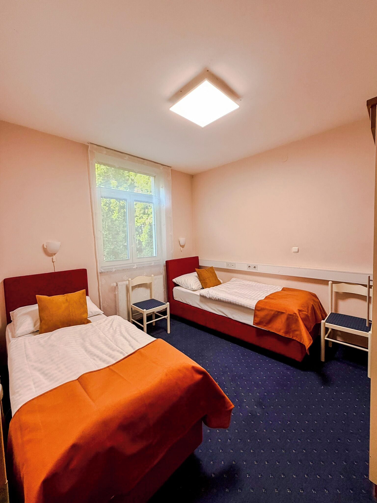 Ein Zimmer mit zwei Betten, einem Fenster, einem Schreibtisch und einem Stuhl.