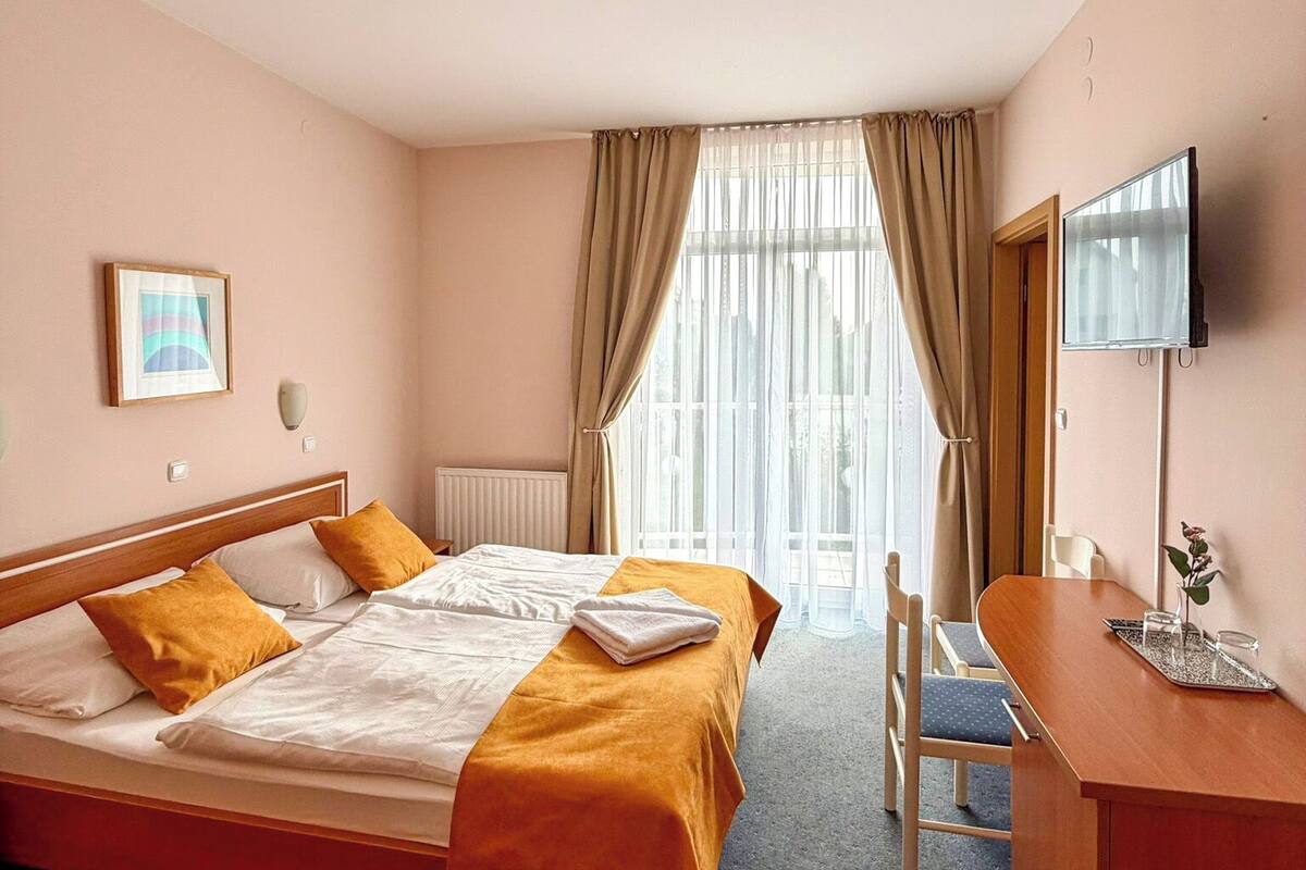 Ein Hotelzimmer mit Bett, Schreibtisch, Stuhl, Fernseher und einem Fenster mit Vorhängen.