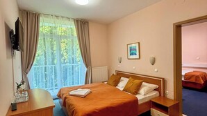 A hotel room with a bed, bedside table, and a view of greenery outside. - Hotel Imperium (Moravske Toplice)