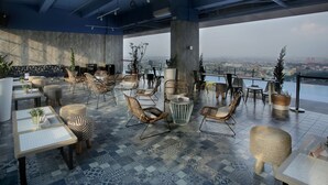 A rooftop lounge with a city view, featuring wicker furniture, patterned flooring, and large windows. - The Zuri Palembang (Palembang)