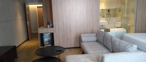 A modern hotel room with a light-colored sofa, a small black table, and a minibar.