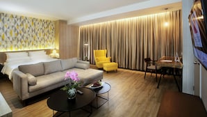 A hotel room with a bed, sofa, yellow armchair, dining table, and a TV. - The Zuri Palembang (Palembang)