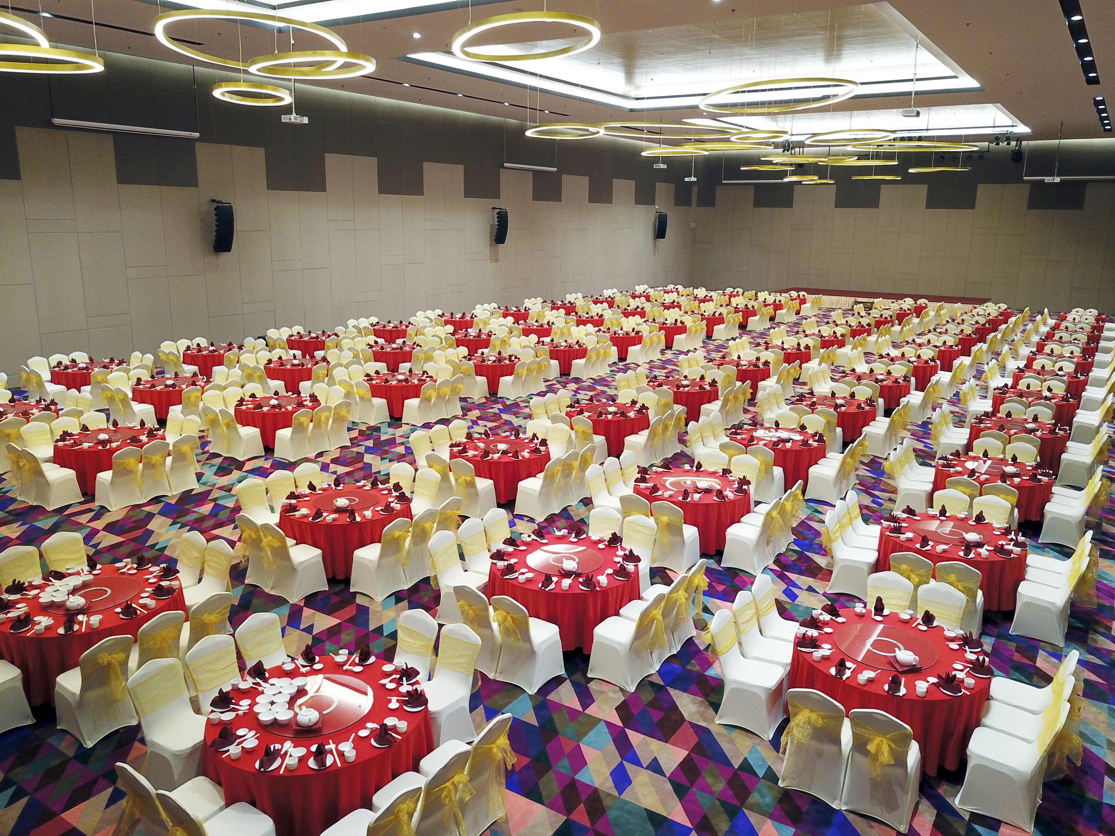 A banquet hall with rows of round tables, each set with white chairs and red tablecloths.