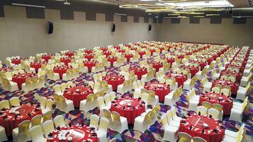 A banquet hall with rows of round tables, each set with white chairs and red tablecloths.