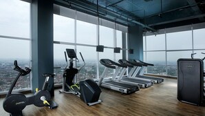A gym with cardio machines, a weight bench, and a large window overlooking a cityscape. - The Zuri Palembang (Palembang)