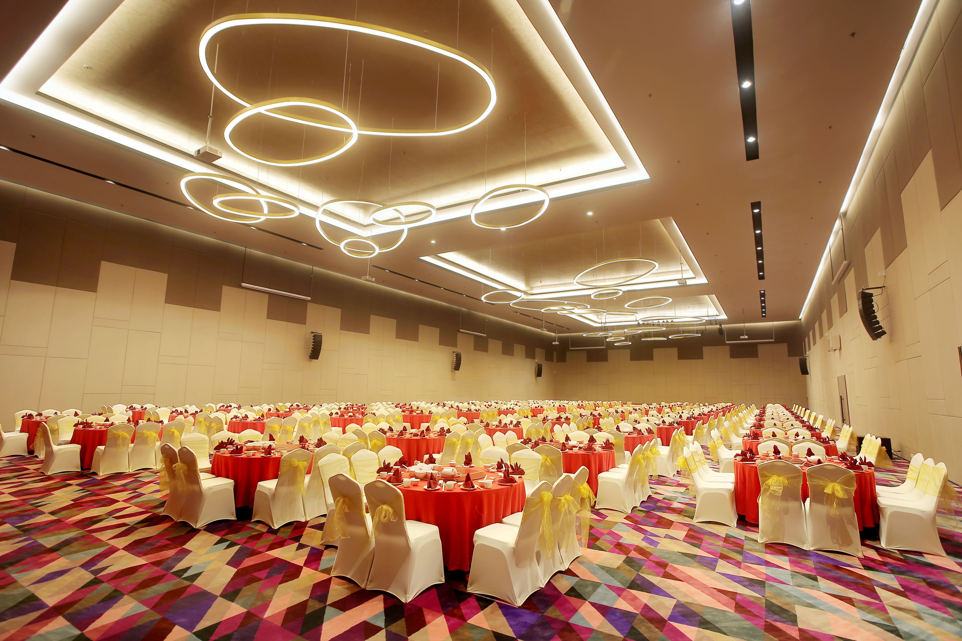A large conference room with rows of tables and chairs, each with red tablecloths and white chairs with yellow sashes.