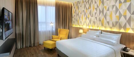 A hotel room with a large bed, a yellow armchair, a TV, and a geometric-patterned wall.