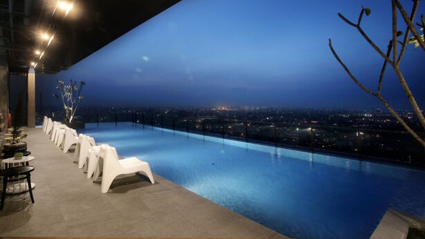 An infinity pool with white chairs and tables, overlooking a cityscape at night. - The Zuri Palembang (Palembang)