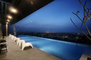 An infinity pool with white chairs and tables, overlooking a cityscape at night. - The Zuri Palembang (Palembang)