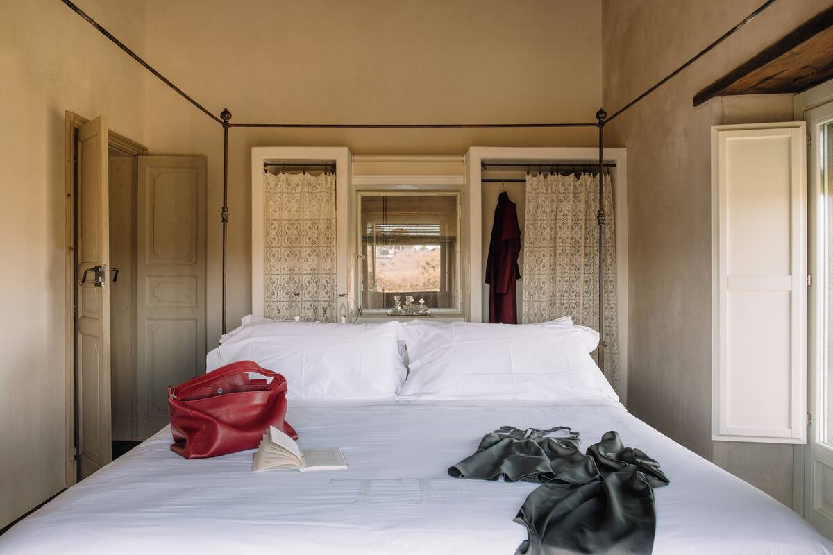 A hotel room with a bed, a red handbag, and a book on the bed.