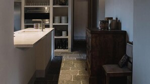 Una cocina estrecha con suelo de piedra, armarios blancos y un banco de madera.
