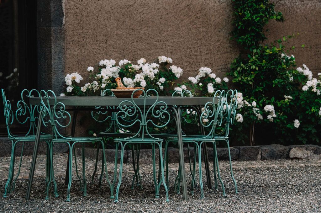A green metal table with chairs set outdoors, surrounded by white flowers and greenery.