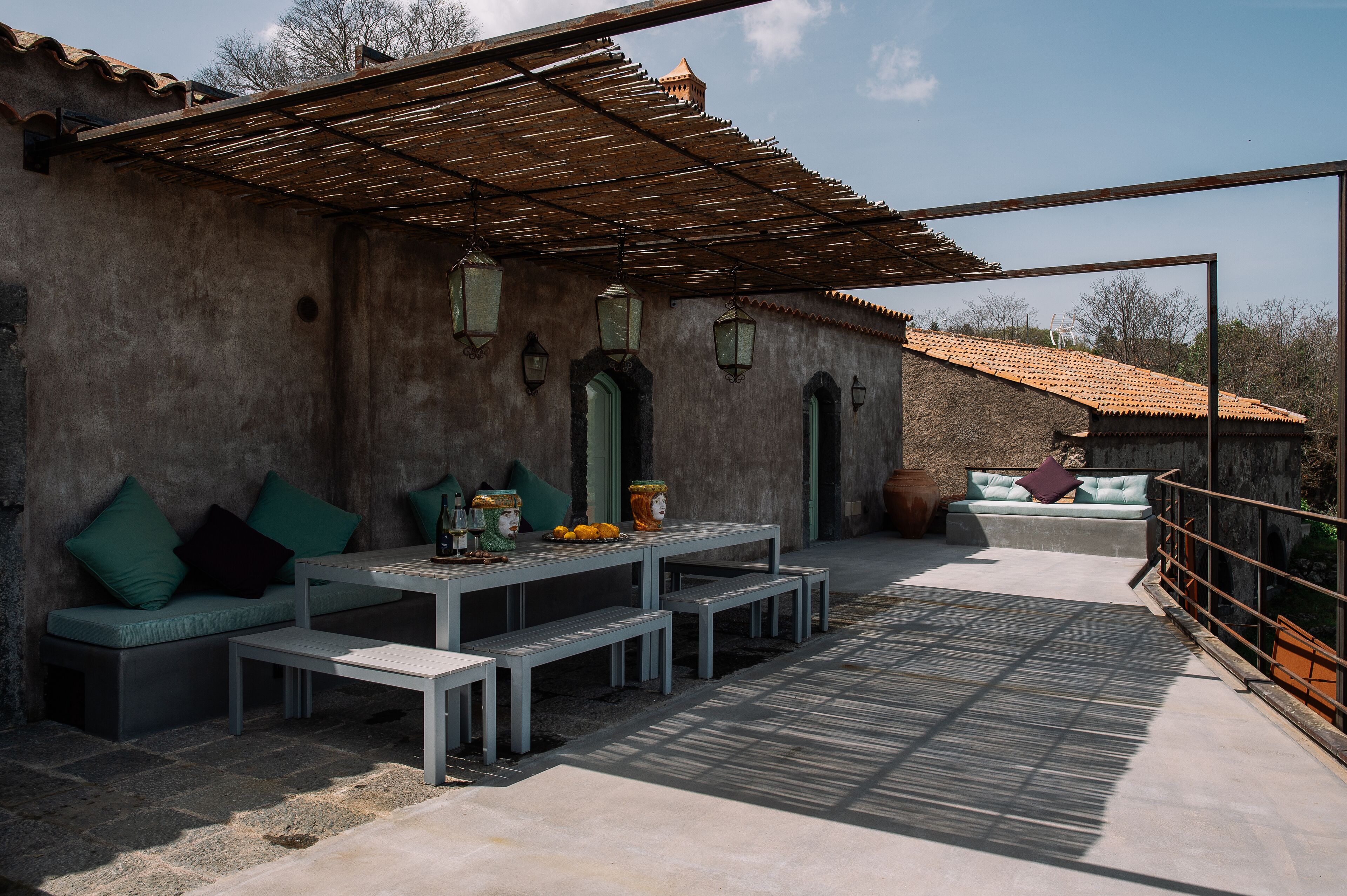 An outdoor patio with a table and benches, a cushioned seating area, and a pergola.