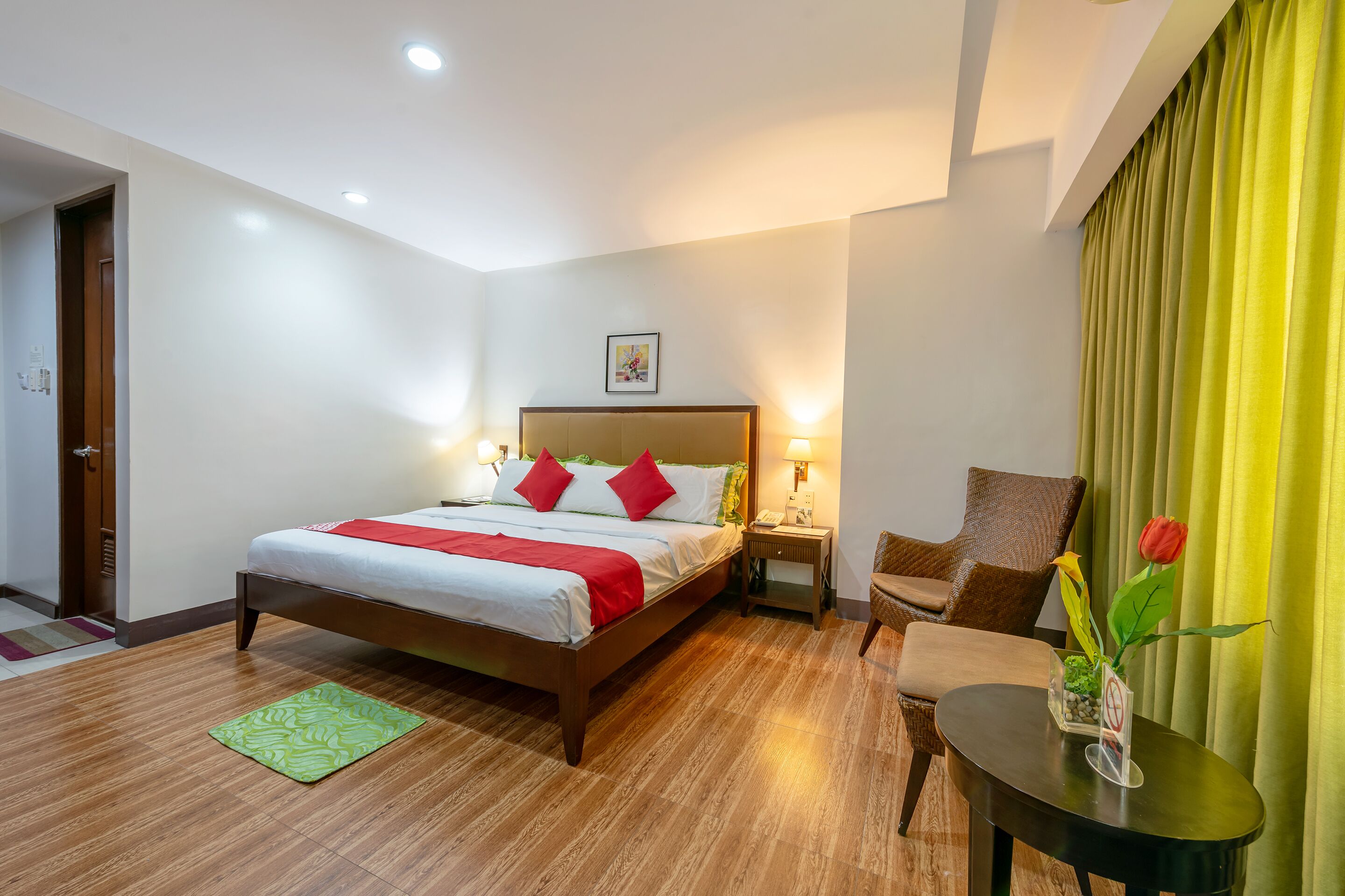 A hotel room with a bed, bedside tables, a chair, a small table with a vase, and a curtain.