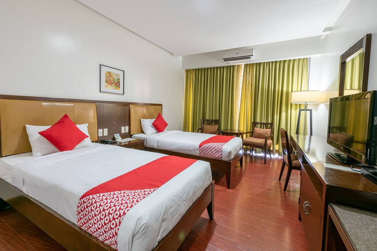 A hotel room with two beds, a desk, a TV, and a chair.