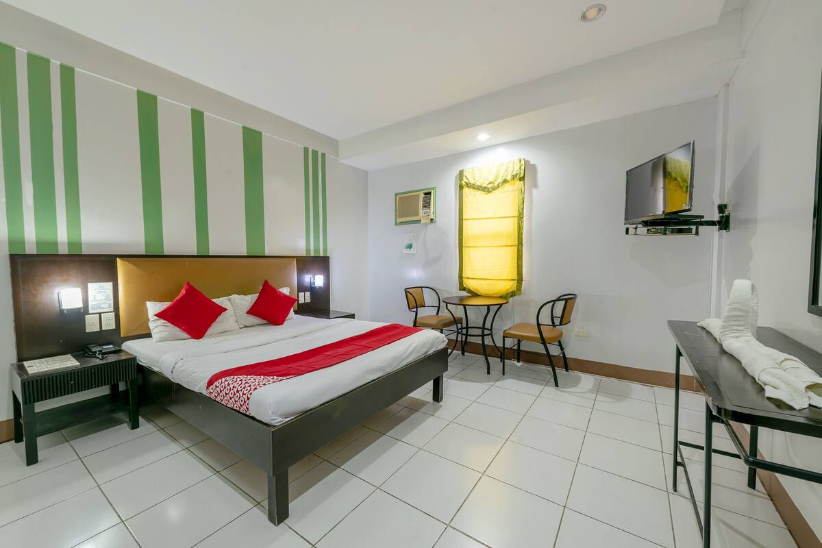 A hotel room with a bed, bedside table, chair, and a small table with a TV.