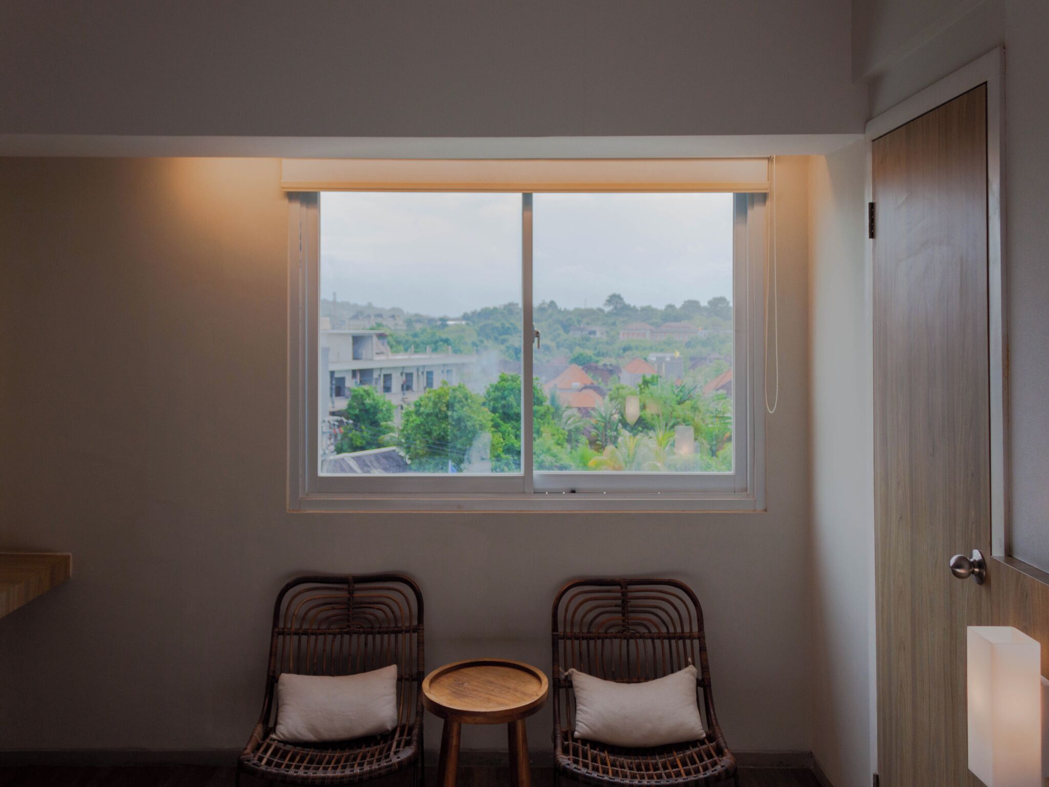 A room with a large window, two wicker chairs, a small round table, and a wooden door.