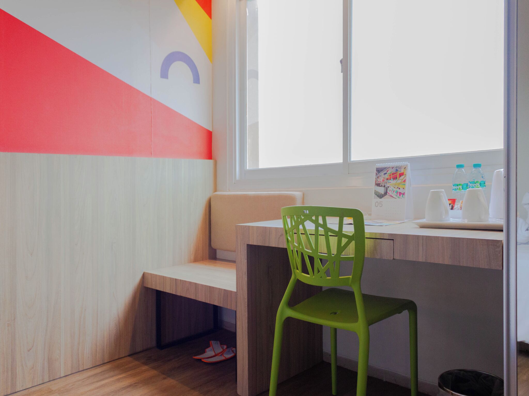 Een moderne kamer met een houten bureau, een groene stoel, een raam met uitzicht en een kleurrijke wand.