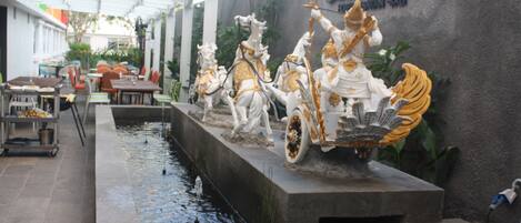 A decorative water feature with statues of riders on horses, a dining area with tables and chairs, and a wall with the text "ZOO EXPRESS".