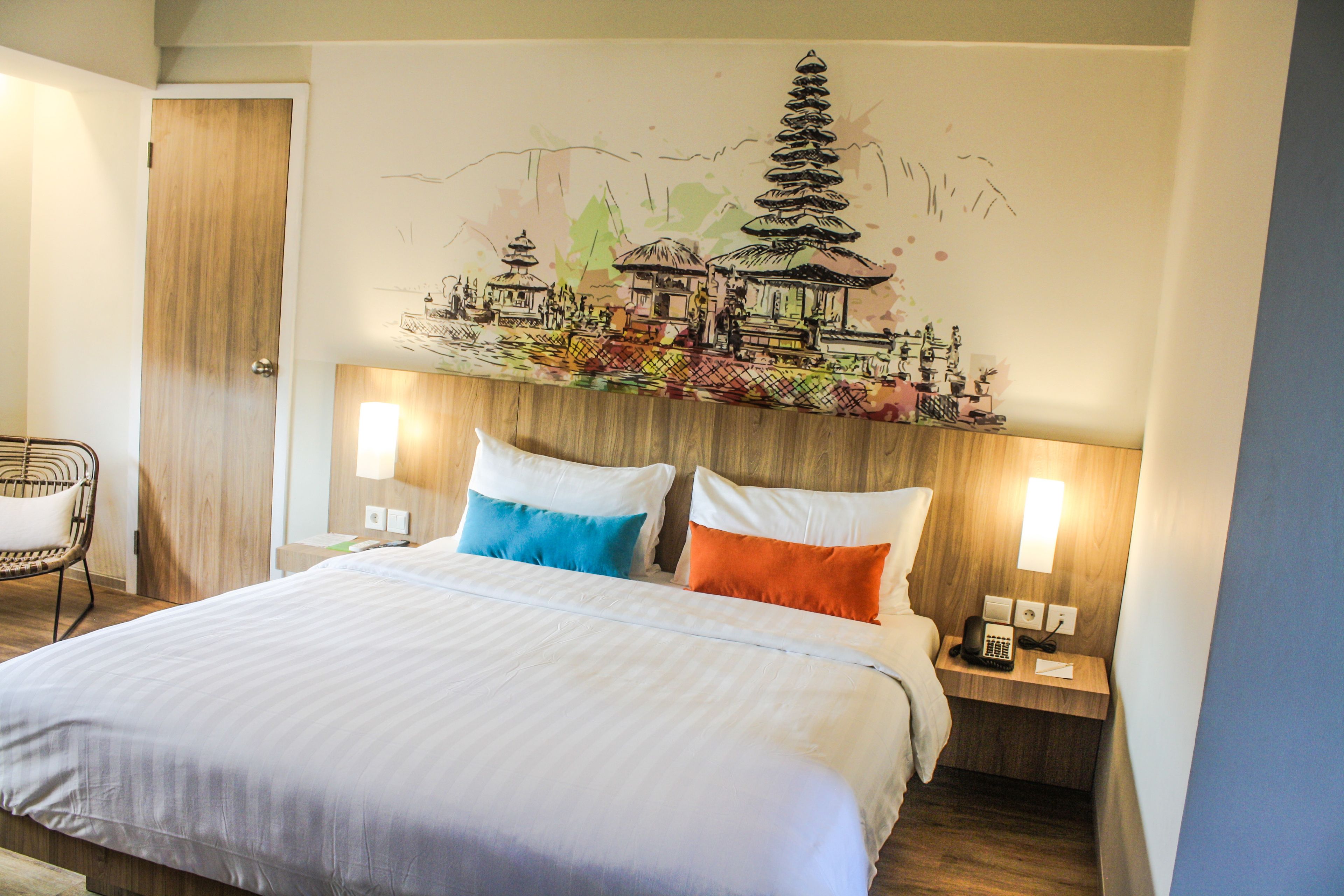 A hotel room with a bed, two bedside lamps, a wooden headboard, and a wall mural.