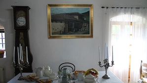 Une table à manger recouverte d’une nappe blanche, entourée de différents plats, d’une horloge et d’un tableau encadré.