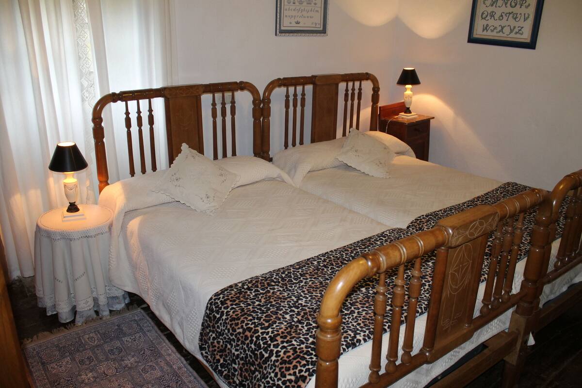 Een netjes opgemaakt bed met een houten hoofdbord, twee bedlampen en een lijst met het alfabet op de muur.