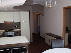 A modern kitchen with white cabinets, a built-in oven, and a gas stove. There is a dining area with a white table and chairs. - Villa Palma (Avella)