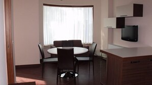 A modern living room with a round dining table, dark chairs, a chandelier, a TV mounted on the wall, and a large window with sheer curtains. - Villa Palma (Avella)
