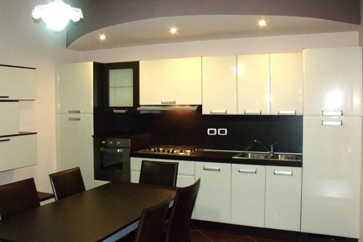 A modern kitchen with white cabinets, a black countertop, and a dining area with a table and chairs.