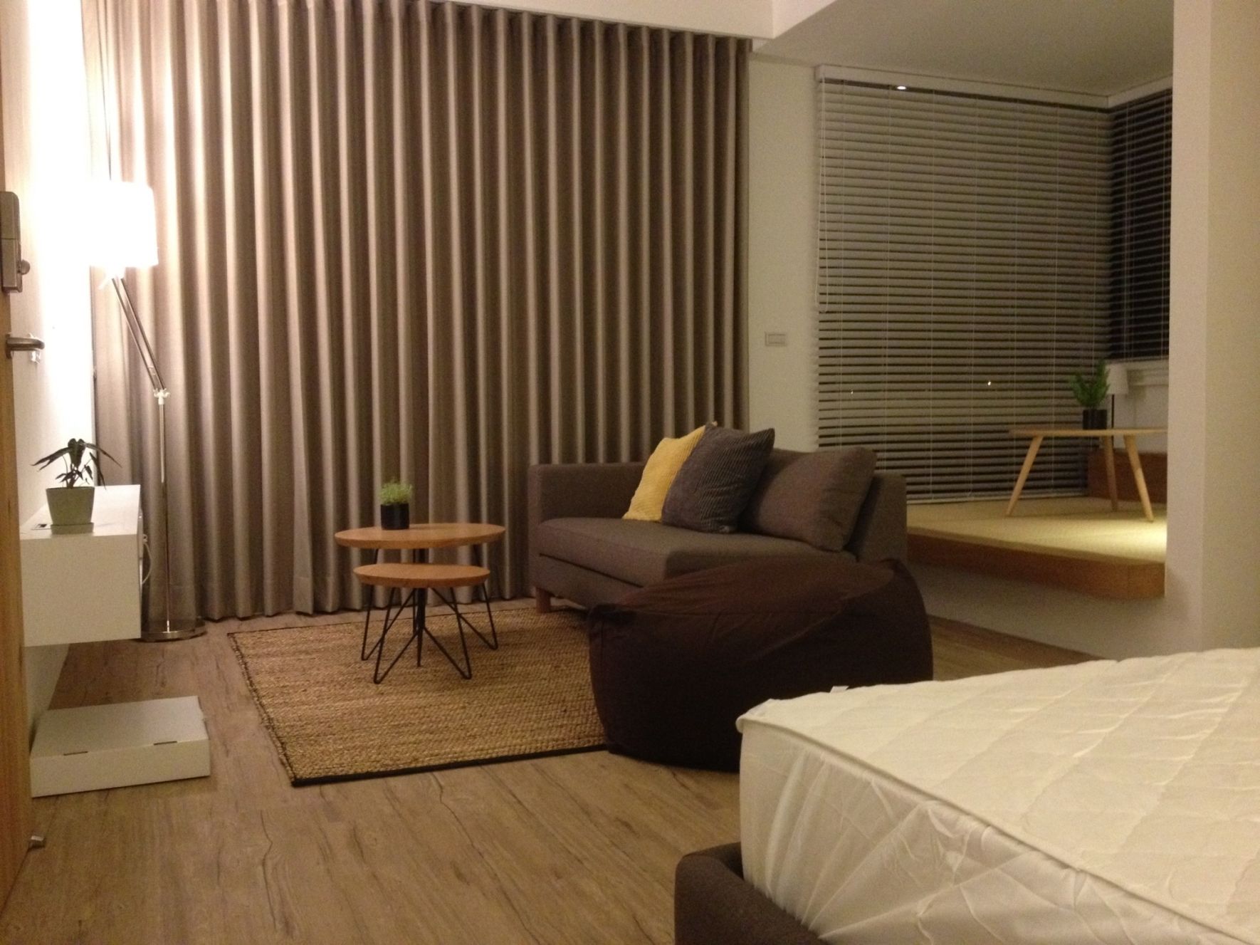Una habitación de hotel moderna con sofá, una mesita redonda, cama y un ventanal grande con persianas.