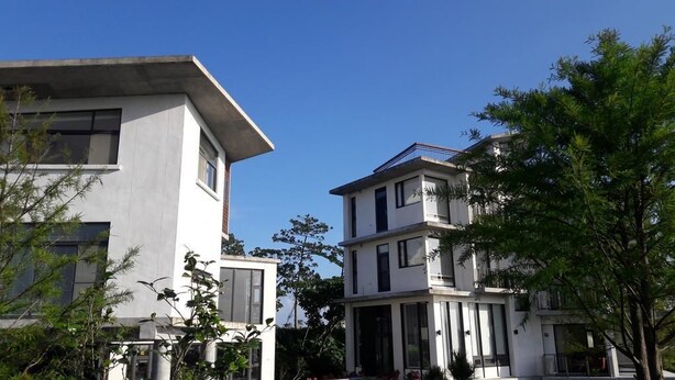 A modern multi-story building with large windows and balconies, surrounded by greenery. - Missy House (Wujie)
