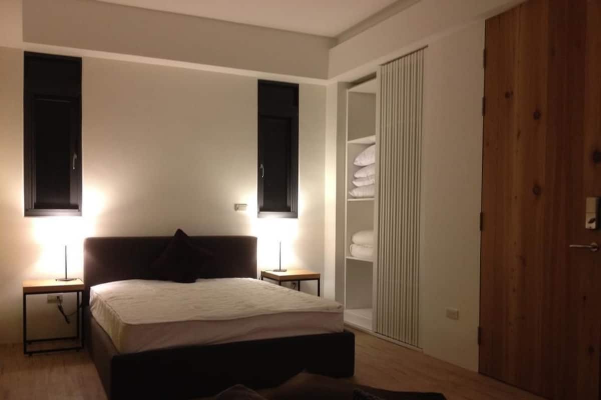 A bedroom with a bed, bedside lamps, a wardrobe, and a wooden door.