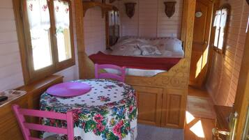 A cozy cabin interior with a wooden bed, a table with a floral tablecloth, and a chair.