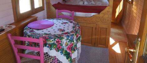 A cozy cabin interior with a wooden bed, a table with a floral tablecloth, and a chair.