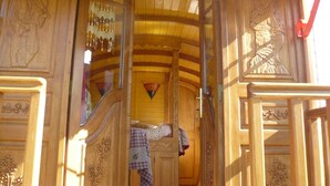 Interior de madera con detalles tallados, una cama con manta a cuadros y una lámpara colgante.