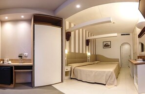 Habitación de hotel compacta con cama, mesitas de noche, escritorio y una pequeña kitchenette.