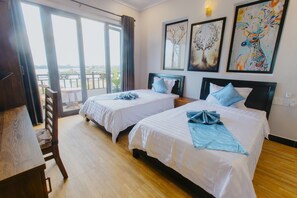 A hotel room with two beds, a wooden desk, and a view of the outdoors. - Home River Villa (Da Nang)