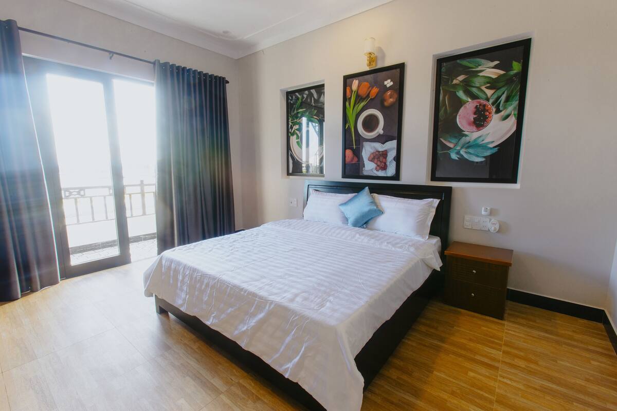 A hotel room with a large bed, a nightstand, and a window with curtains.